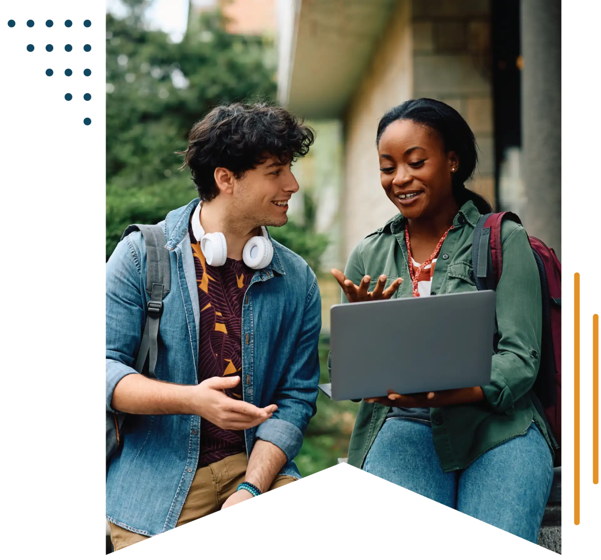 Two college students sitting on a stone wall discussing something they see on a laptop screen.