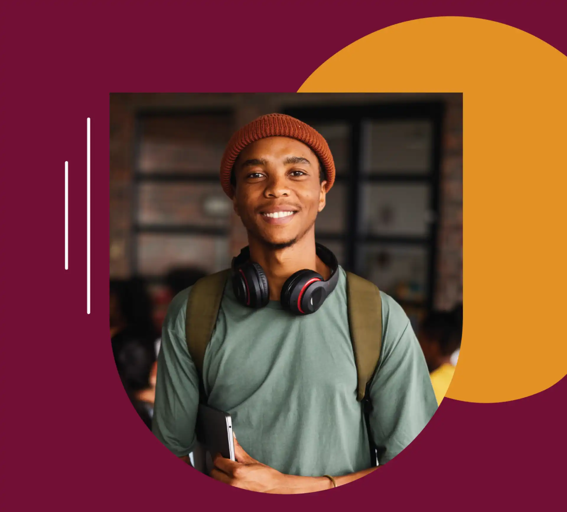 A smiling young man in an orange knit beanie with wireless headphones around his neck and a laptop under his arm.